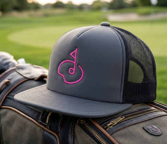 Charcoal golf trucker hat with pink embroidery and a mesh back, shown from the front on a light background